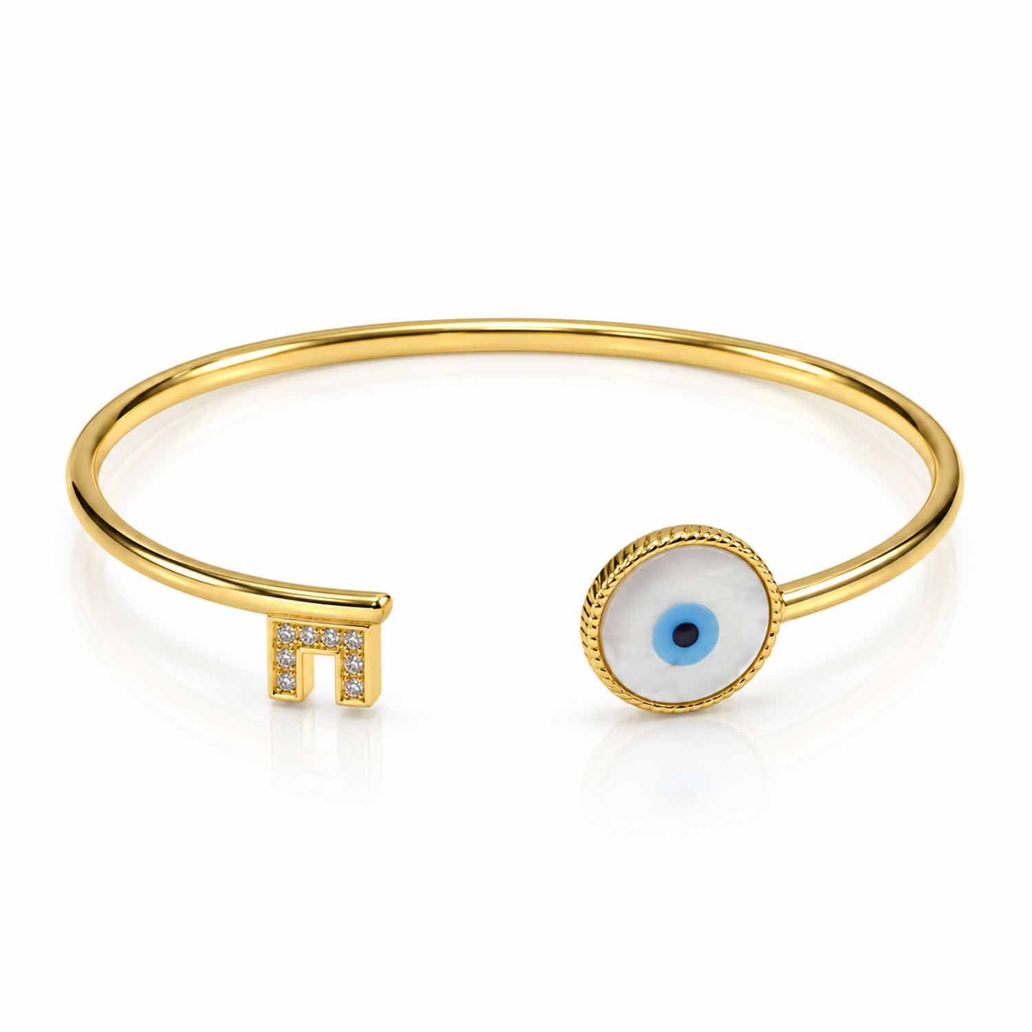 Gold open cuff bangle featuring a round blue evil eye centerpiece with a textured gold border and a crystal-studded geometric end detail, displayed on a clean white background.