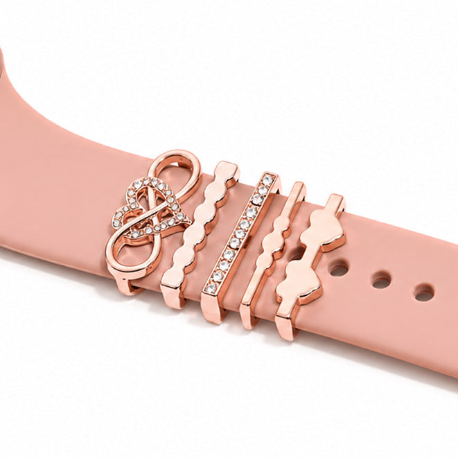 Rose gold smartwatch strap decorated with a sparkling peace symbol charm, wavy rose gold bands, and a pavé crystal bar on a white background.