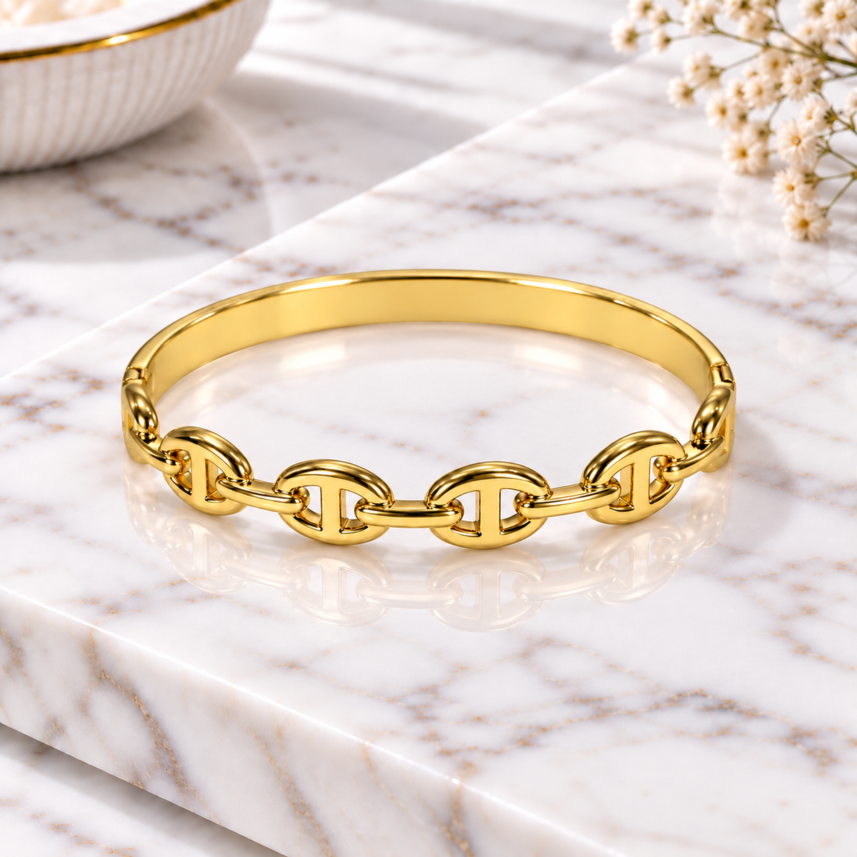 Gold-tone chain-link bangle bracelet displayed on a white marble surface with soft floral decor.
