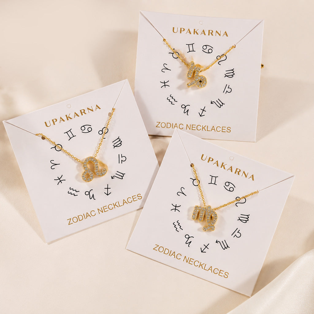 Gold-plated zodiac necklace collection displayed on Upakarna zodiac cards, featuring sparkling zodiac-symbol pendants, delicate gold chains, and a premium beige-and-white presentation.