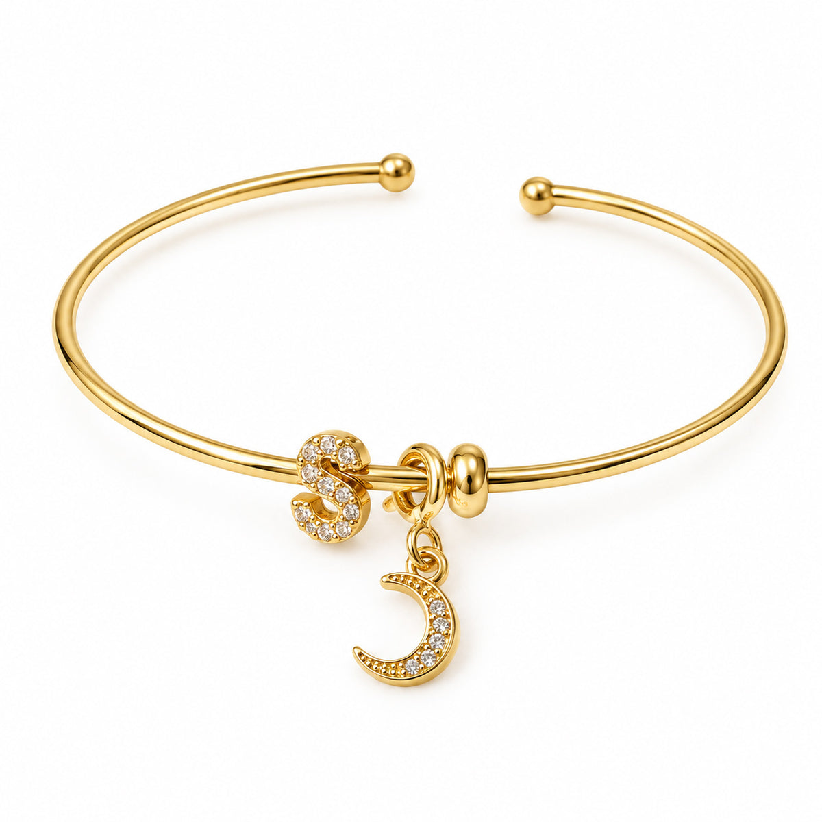 Gold open cuff bangle featuring a sparkling letter S charm and a crystal crescent moon charm on a clean white background.