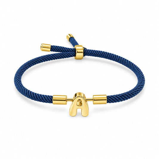 Gold-tone initial “A” charm bracelet with a navy blue braided cord and adjustable sliding closure, displayed on a clean white background.