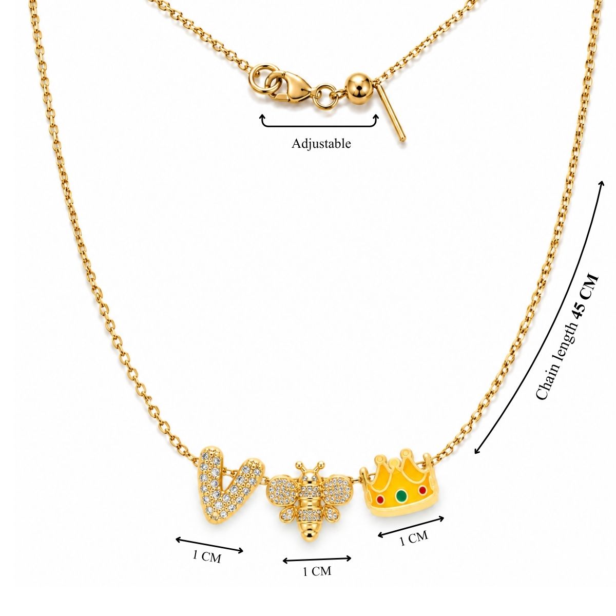 Product measurement image showing a 45 cm gold chain necklace with an adjustable slider mechanism and three 1 cm charms: a crystal-paved letter "V", a gold bee with crystals, and an enamel crown with red and green details.