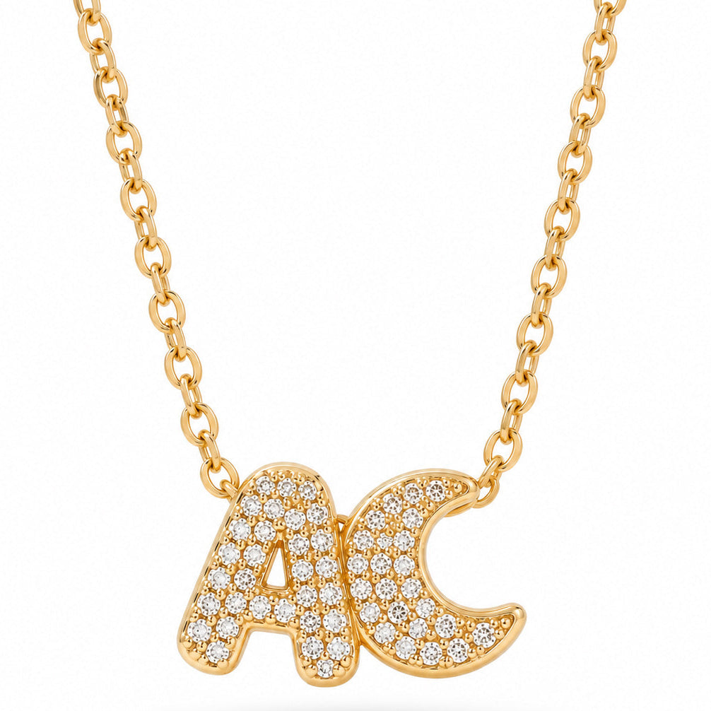 A studio product shot showing a delicate gold link necklace featuring sparkly pave-set rhinestone charms spelling "A" and "moon"