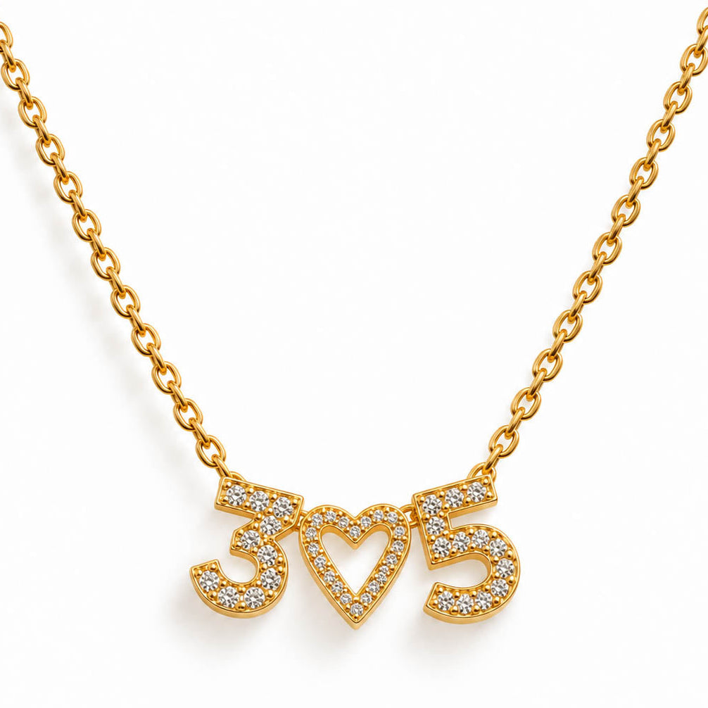 A studio shot of a thin gold link necklace centered with three rhinestone-encrusted charms spelling out the number "3", an open heart, and the number "5".