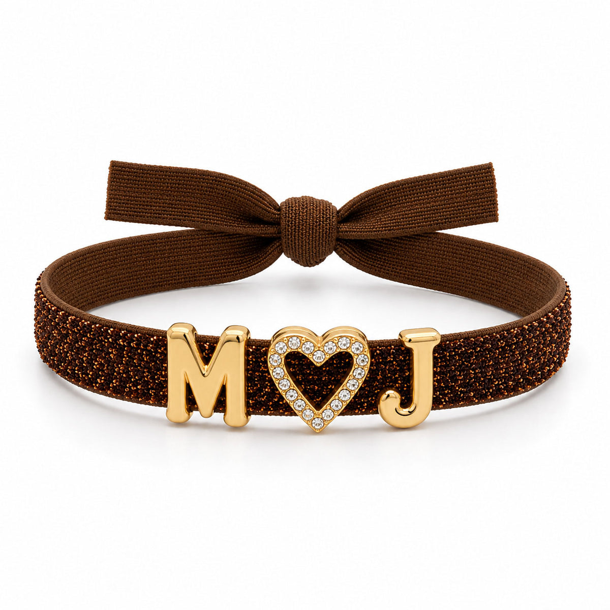 Brown glitter bracelet with a matching fabric bow, featuring gold “M” and “J” initial charms with a crystal-studded heart charm in the center, displayed on a clean white background.