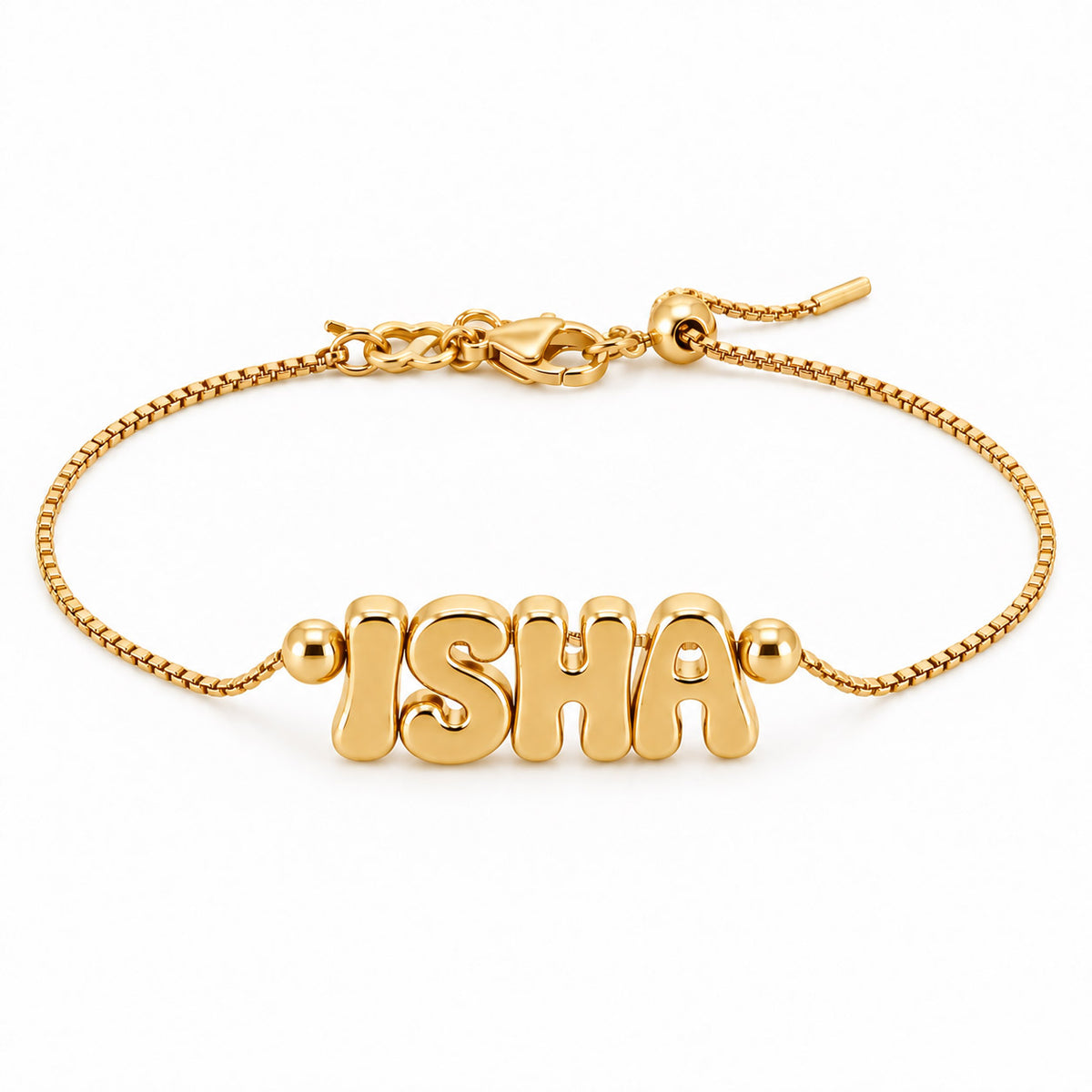 A product studio photograph of a gold-toned adjustable box-chain bracelet featuring chunky, puffed bubble-letter charms spelling "ISHA" flanked by smooth gold beads, displayed against a solid white background with a lobster clasp and slider mechanism visible.