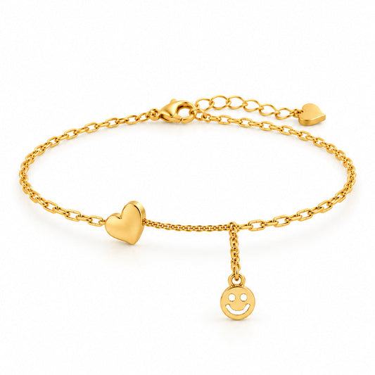 Gold-tone adjustable anklet featuring a polished heart charm and a dangling smiley face pendant, finished with a delicate chain and a small heart-shaped extender tip, displayed on a clean white background.