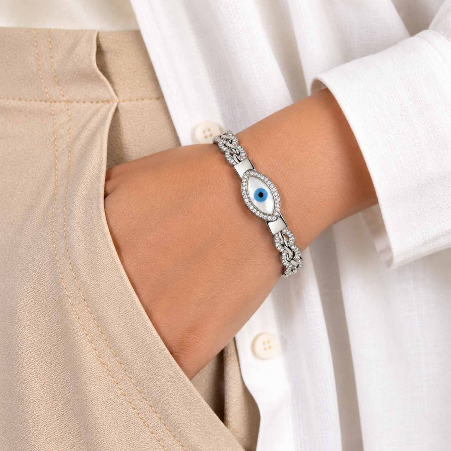 Silver crystal evil eye cuff bangle with a blue eye centerpiece, worn on the wrist with a neutral outfit.