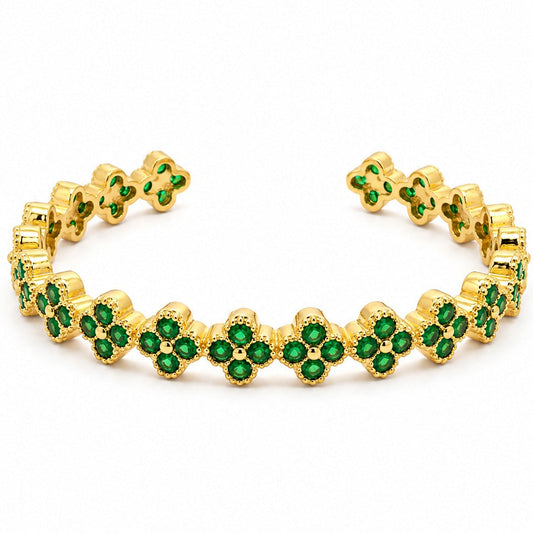 Anti-tarnish yellow gold open cuff bracelet featuring a continuous band of four-leaf clover quatrefoil links, each pave-set with round green emerald cubic zirconia stones and finished with beaded milgrain edges, set against a solid white background.