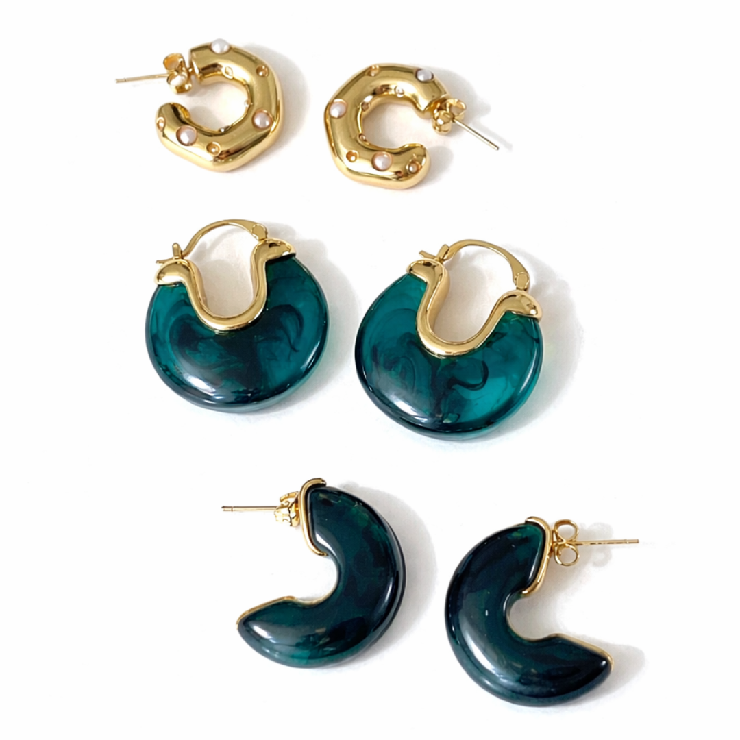 Three-pair earring stack featuring deep emerald green resin hoops, gold half-hoops, and a crystal bow earring with a large drop pearl on a branded card.