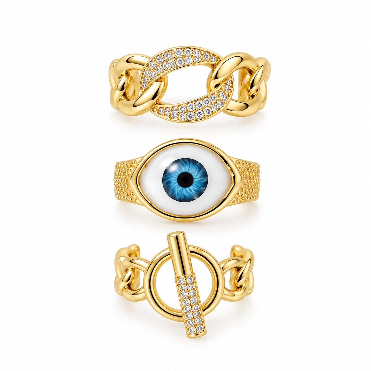 Three gold statement rings featuring a chunky pavé chain-link ring, a bold blue evil eye ring, and a toggle chain ring with sparkling crystal details on a clean white background.
