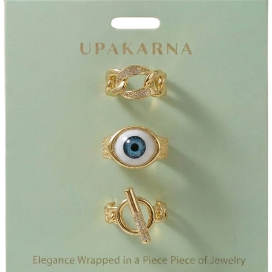 A stack of three adjustable gold-toned rings: a sculptural spike spiral, a chunky chain-link band, and a central signet ring featuring an evil eye symbol.