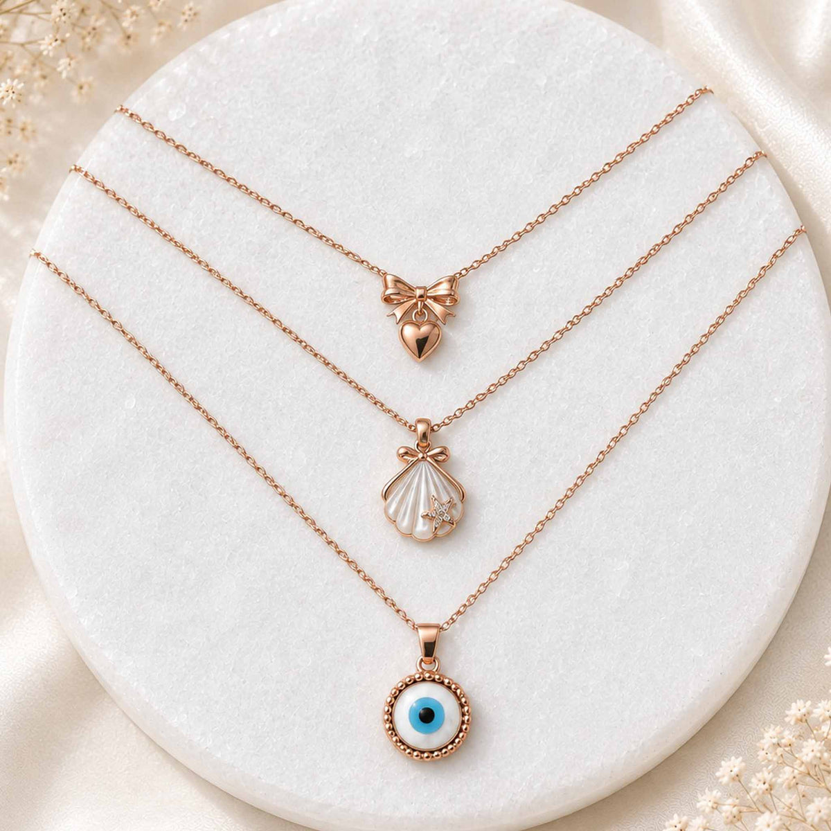 Gold layered necklace set with bow heart, pearl shell, and blue evil eye pendants displayed on a white circular jewellery stand.