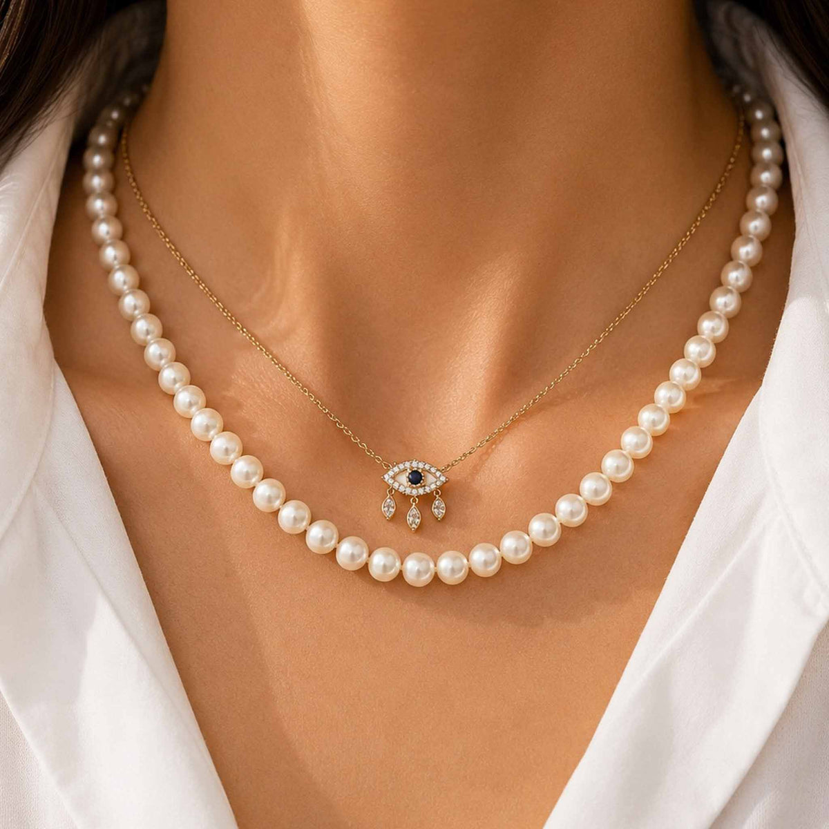 Layered pearl necklace and delicate gold evil eye pendant necklace styled on a model wearing a white outfit.