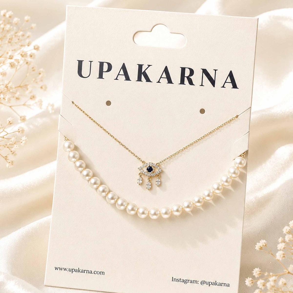 Gold evil eye pendant necklace paired with a pearl strand necklace displayed on a white circular jewellery stand.