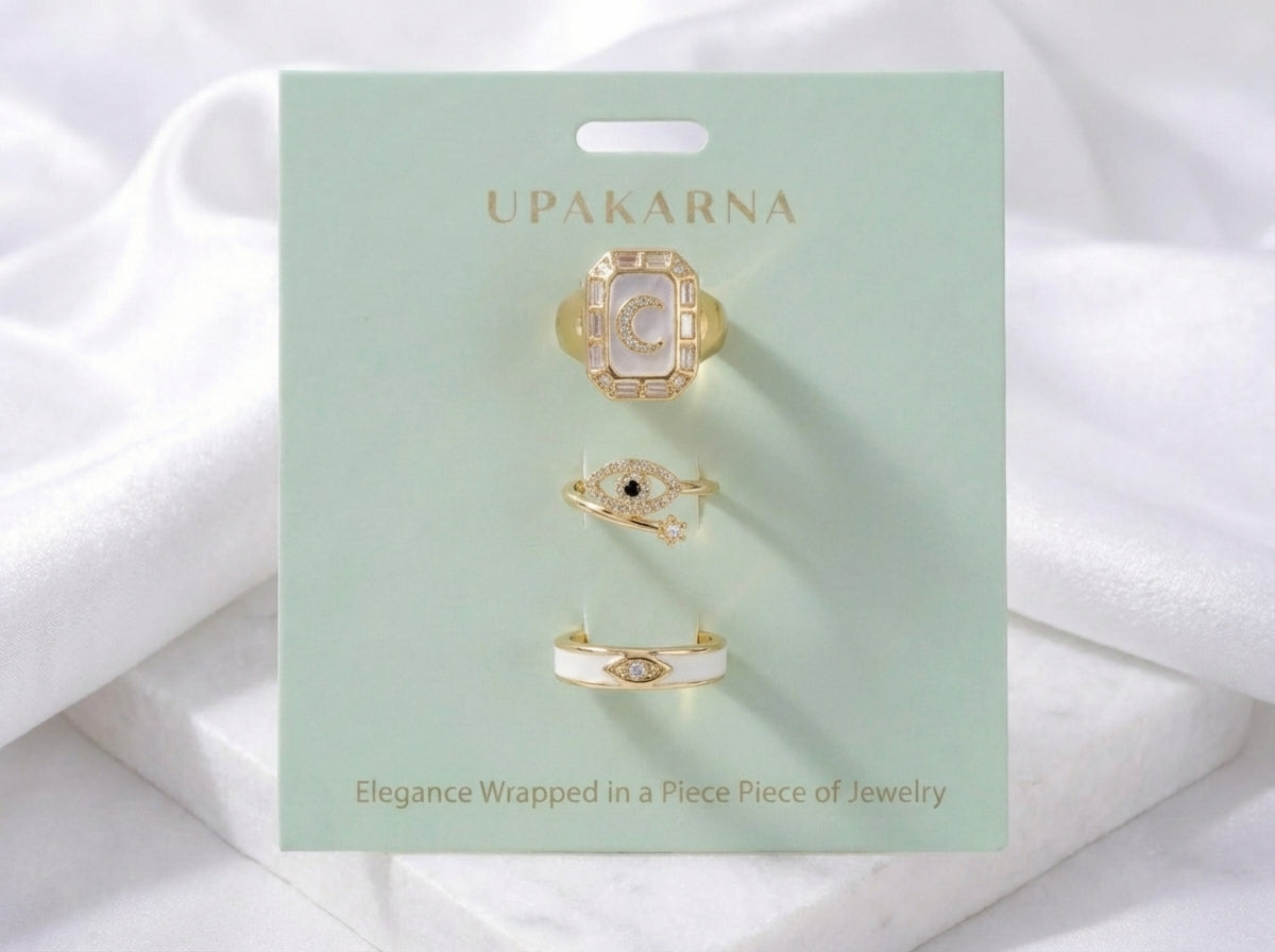 Gold-tone ring stack with ivory enamel band, blue moon ring, and evil eye rings with crystal detailing
