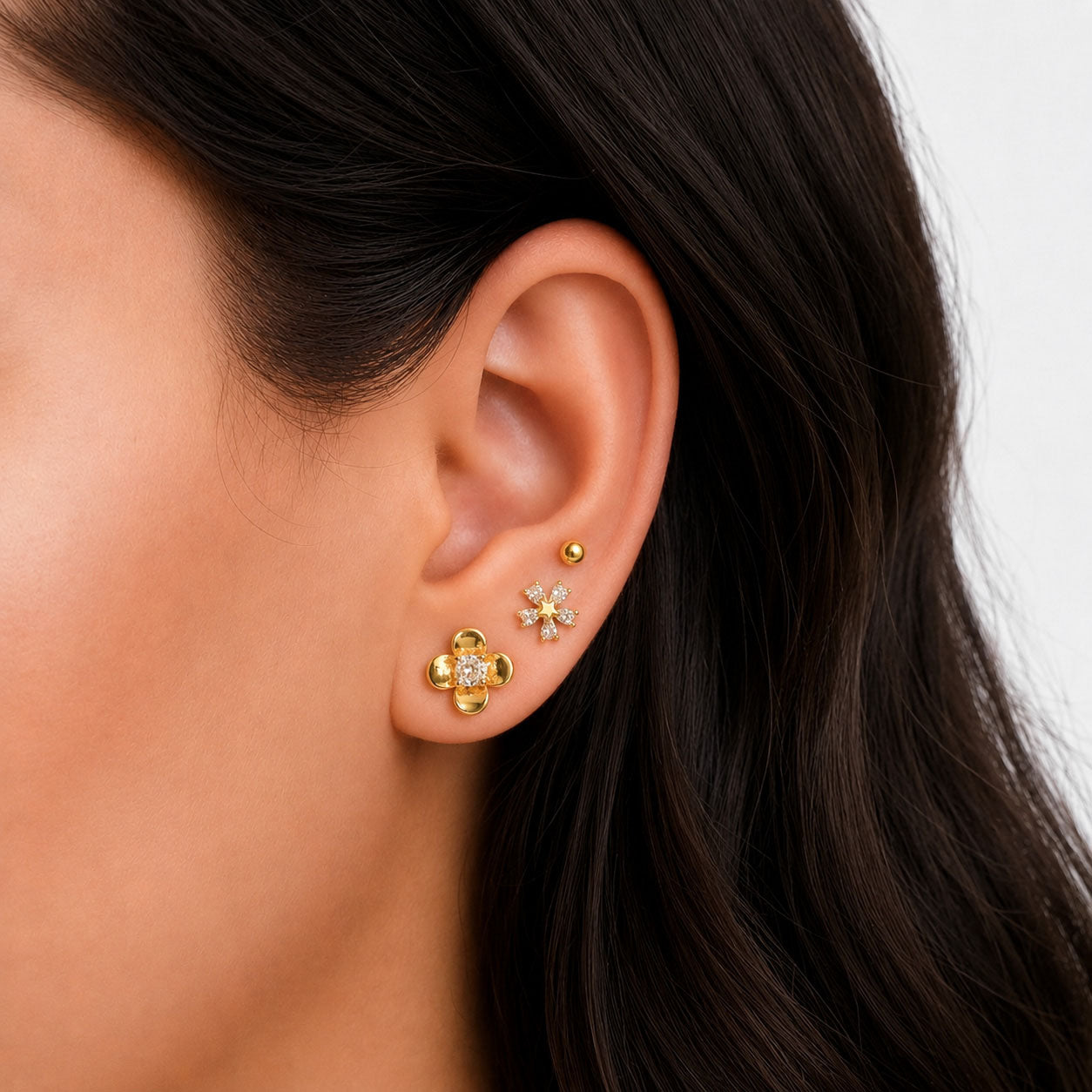 Zoomed-out view of three pairs of gold earrings on a white background, featuring gold ball studs, crystal-centered floral studs, and crystal snowflake-shaped studs.