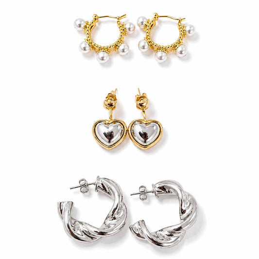 Gold, silver and pearl earring stack featuring pearl-detailed hoops, two-tone heart drop earrings and sculptural twisted silver hoops, displayed on a clean white background.