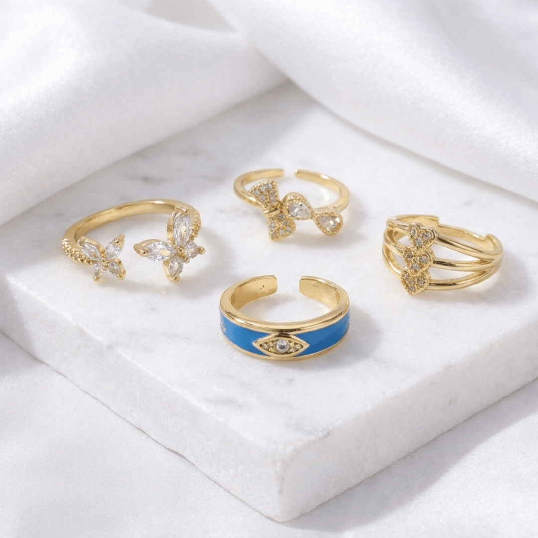 Set of five adjustable gold rings featuring an infinity bow, triple hearts, a textured coil, an enamel butterfly, and a crystal evil eye.