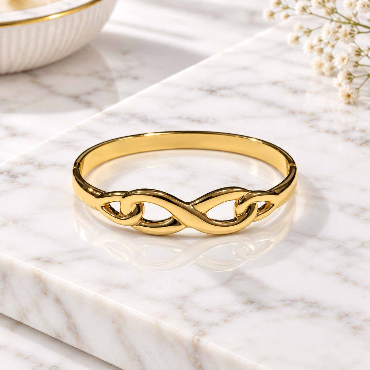 Polished gold-tone infinity design bangle displayed on a marble surface.