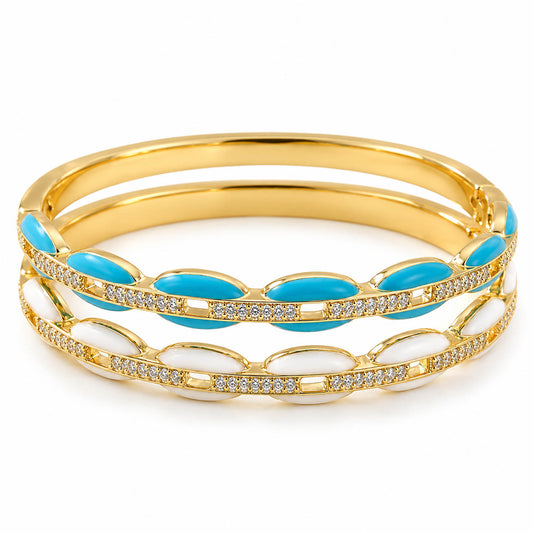 A product photo of a stacked set of gold-tone bangles featuring enamel stations in turquoise and white alongside rhinestone-paved accents.