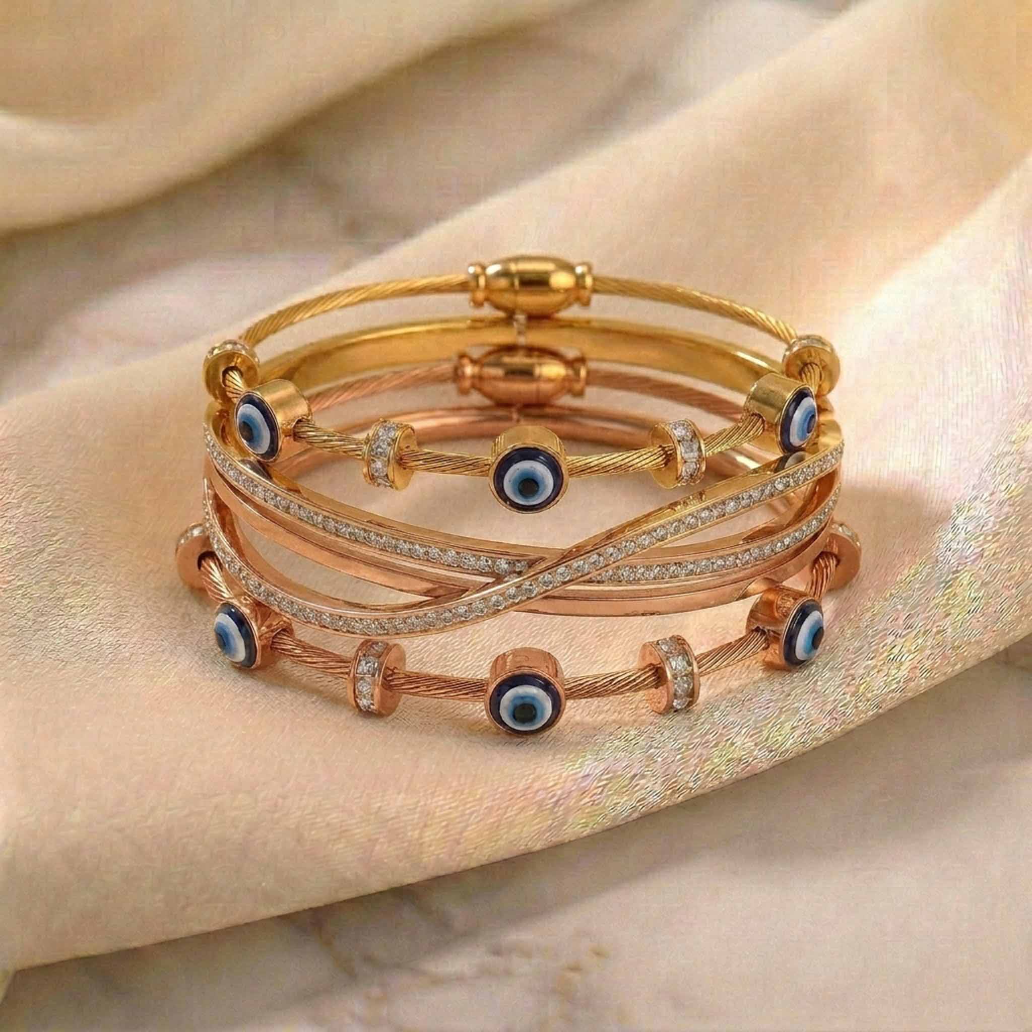 Luxury gold and rose gold anti-tarnish bracelet stack featuring crystal crossover bangles, blue evil eye cable bracelets, and sparkling crystal accents, elegantly displayed on soft satin fabric