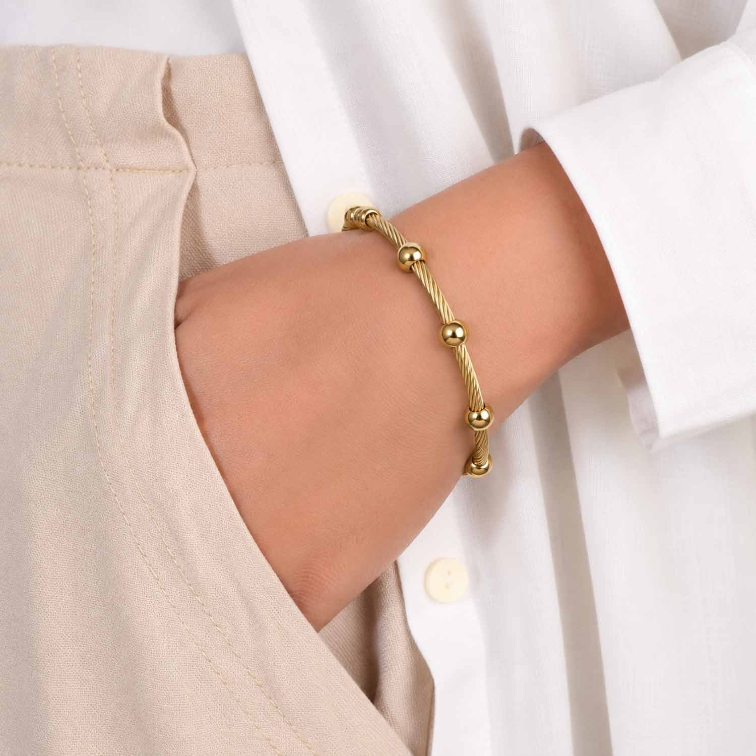 Gold twisted cable cuff bangle with polished bead accents, worn on the wrist with a neutral outfit.