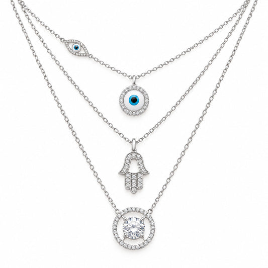 Upakarna silver layered necklace set featuring an evil eye chain, crystal evil eye pendant, Hamsa hand pendant, and solitaire circle pendant on a clean white background.