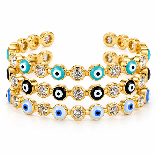 A product photo of a stacked set of gold-tone open cuff bracelets featuring alternating crystal stones and evil eye charms in turquoise, black, and light blue.