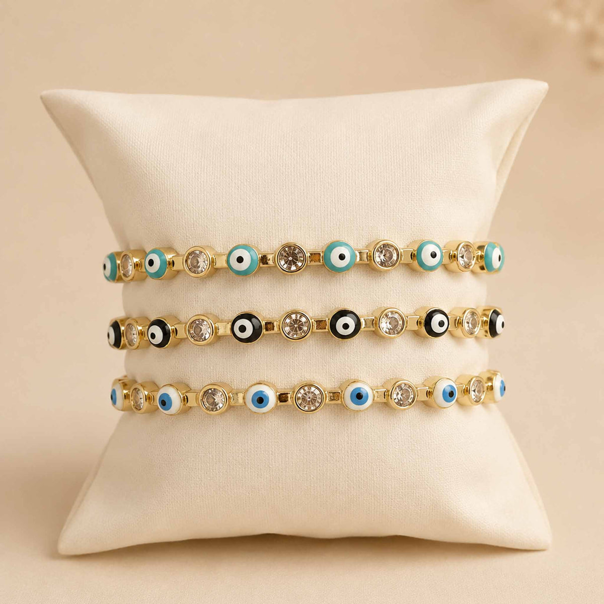 Mystic Blue Stack featuring three gold Evil Eye cuff bangles in light blue, black, and white, displayed on a cream jewellery cushion.