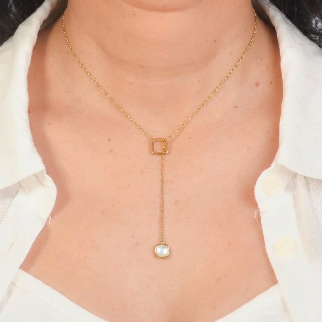Close-up of a model wearing an elegant gold-tone lariat necklace featuring an open square connector and a dangling bezel-set square mother-of-pearl pendant. The anti-tarnish geometric necklace is styled with a white collared shirt, showcasing its modern minimalist design for everyday wear, office outfits, layering, gifting, and special occasi