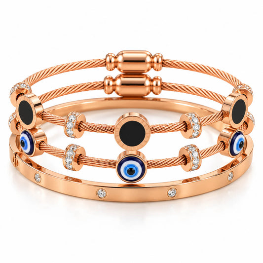 A studio shot of a curated luxury bracelet stack featuring multiple rose gold cable wire strands adorned with black circular enamel stations, blue-and-white evil eye charms, and sparkling rhinestone spacers, paired with a matching gem-set bangle.