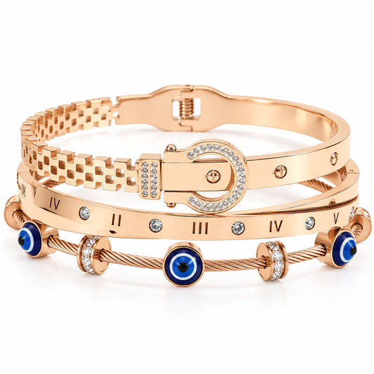 A product photo of a stacked set of rose gold-tone bracelets featuring a buckle-style link bangle, a band engraved with Roman numerals and crystals, and a twisted cable wire bracelet with blue-and-white evil eye charms and rhinestone spacers.