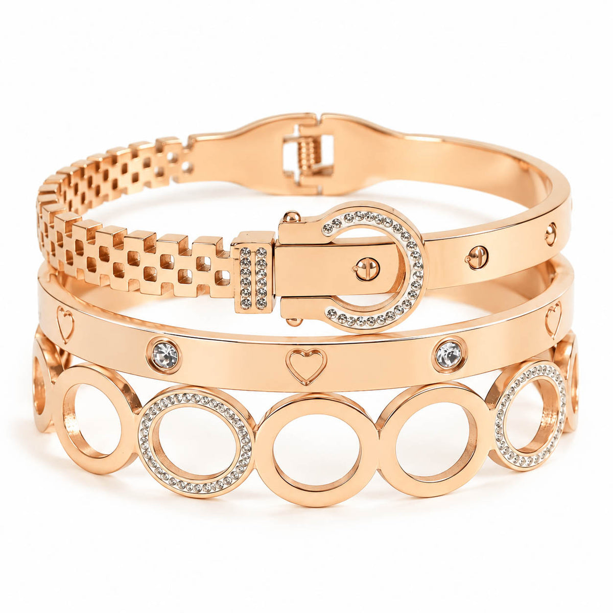 A curated luxury rose gold bracelet stack, showcasing three distinct bangles: an upper textured strap with a rhinestone-paved buckle closure, a middle band engraved with miniature hearts and set with round crystals, and a lower openwork bangle formed by interlocking circular links with crystal-paved rims.