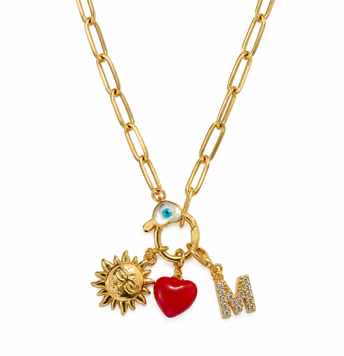 Gold-plated paperclip chain necklace with a blue Evil Eye centerpiece, sun charm, red heart charm, and sparkling “M” initial charm, displayed on a clean white background.