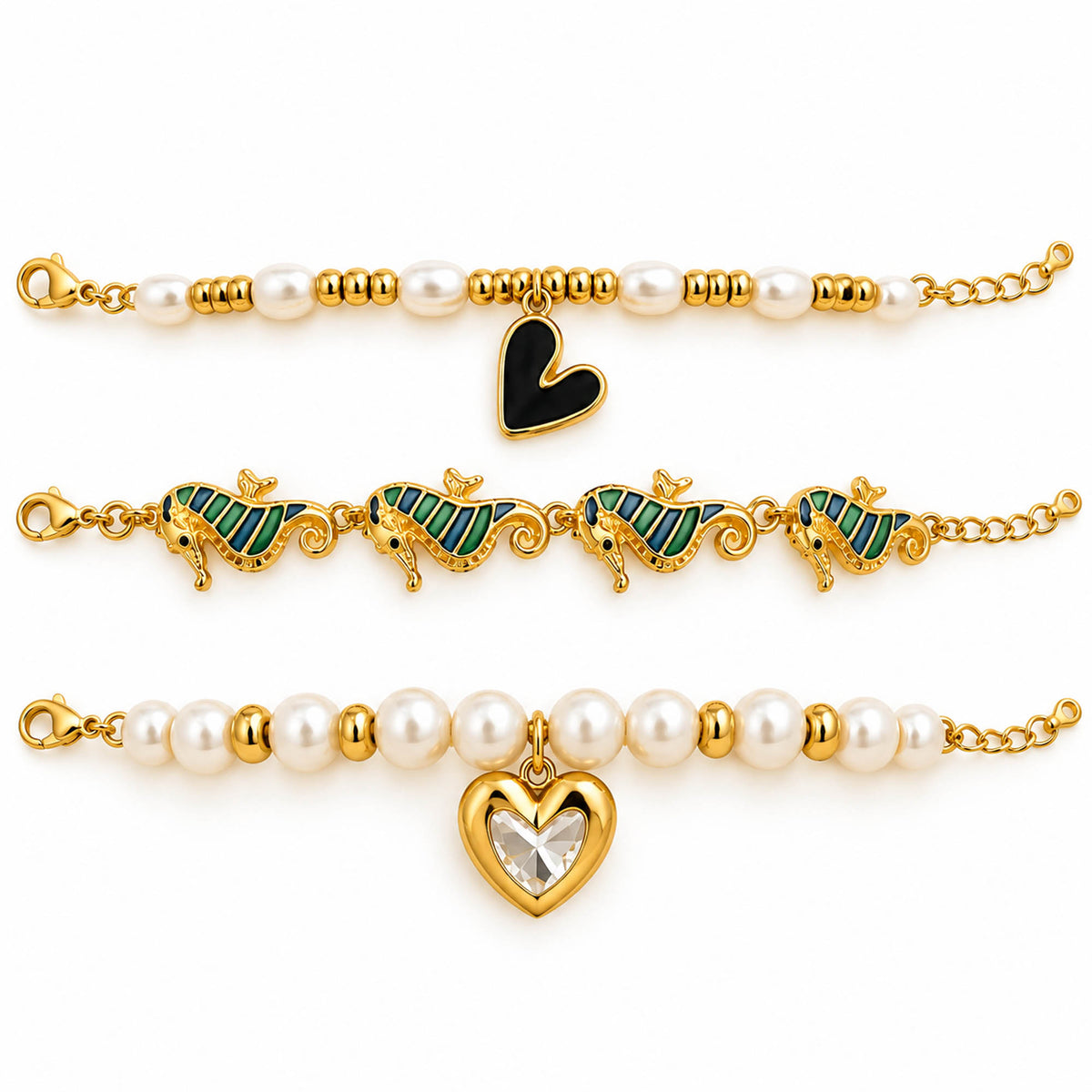 A product photo of a stacked set of gold-tone charm bracelets featuring a pearl strand with a black heart pendant, a link chain of striped seahorse charms, and a pearl strand with a crystal-accented gold heart charm.