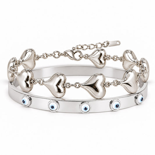 A product photo of a stacked set of silver-tone bracelets featuring a linked chain with smooth puffy heart charms and a solid bangle decorated with blue-and-white evil eye motifs.