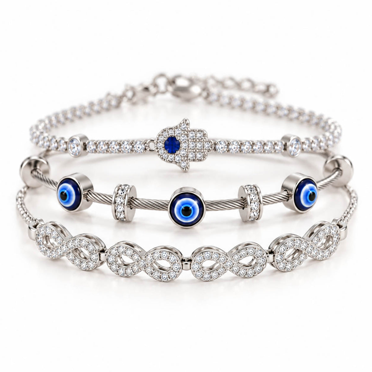 A product photo of a stacked set of silver-tone bracelets featuring a crystal-paved Hamsa hand with a blue stone, a twisted cable wire band with blue-and-white evil eye charms, and a linked infinity symbol bracelet covered in rhinestones.