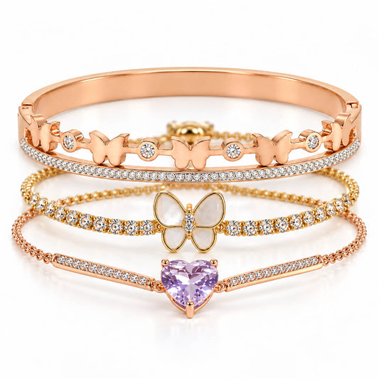A studio shot of a curated luxury rose gold bracelet stack showcasing three distinct pieces: an upper hinged bangle adorned with small butterflies and crystal stones, a middle crystal-paved chain featuring a central white mother-of-pearl butterfly pendant, and a lower thin link chain centered with a faceted pastel purple heart-shaped crystal.
