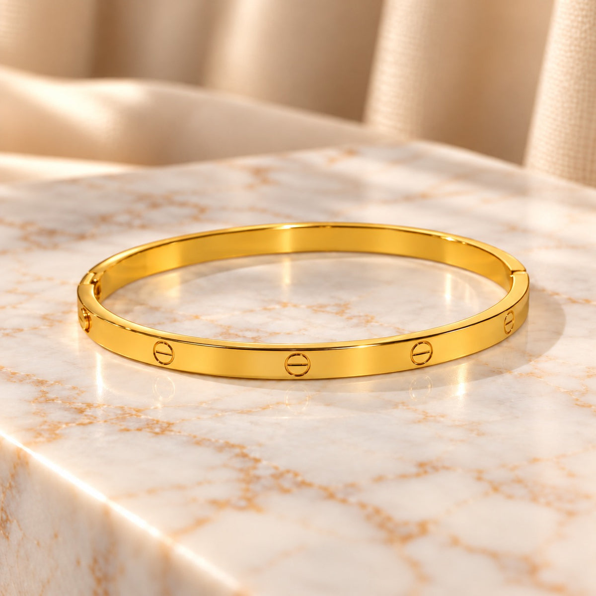 Slim golden anti-tarnish screw-design bangle displayed on a cream marble surface with a soft beige background.