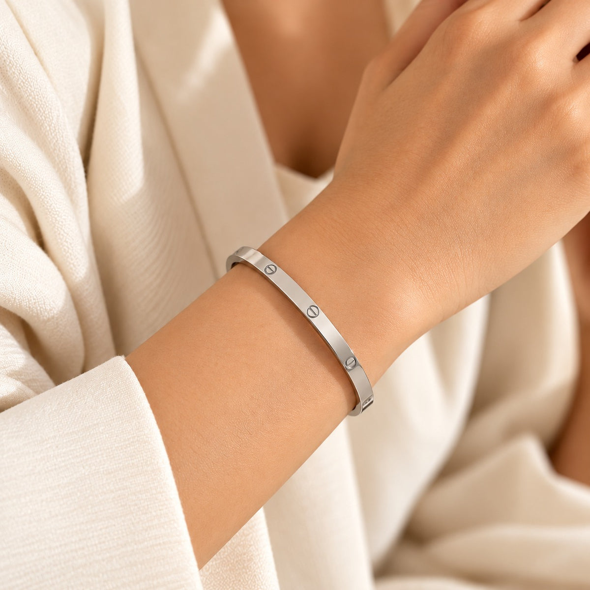 Silver-tone minimalist bangle worn on a woman's wrist, featuring a sleek polished finish and three engraved screw-inspired details, styled with an elegant ivory outfit in warm, soft natural lighting.