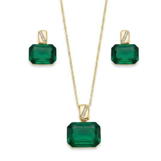A gold jewelry set isolated on a plain white background, featuring a fine-chain necklace with a large emerald-green, emerald-cut gemstone pendant suspended from a polished gold bail with a diagonal pave-set crystal accent. The set is paired with matching stud earrings that replicate the same emerald-cut green stone and pave-accented gold bail design for a sophisticated finish.