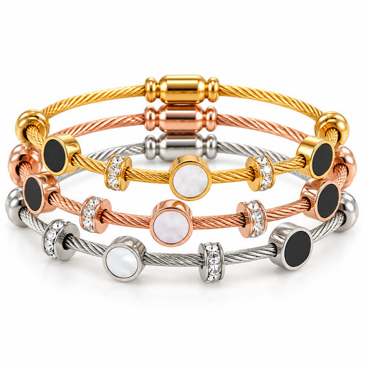 A studio shot of a multi-tone luxury bracelet stack showcasing layered cable wire strands in gold, rose gold, and silver finishes. The set is accented with circular stations featuring black enamel and white mother-of-pearl inlays, interspersed with sparkling crystal-paved ring spacers.