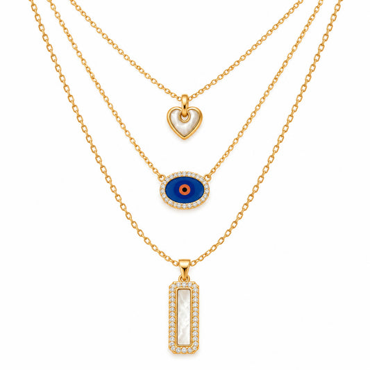 A product photo of a layered gold-tone necklace set featuring a heart pendant with white mother-of-pearl inlay, a horizontal oval evil eye charm framed in crystals, and a rectangular pendant with a mother-of-pearl center and a rhinestone border.