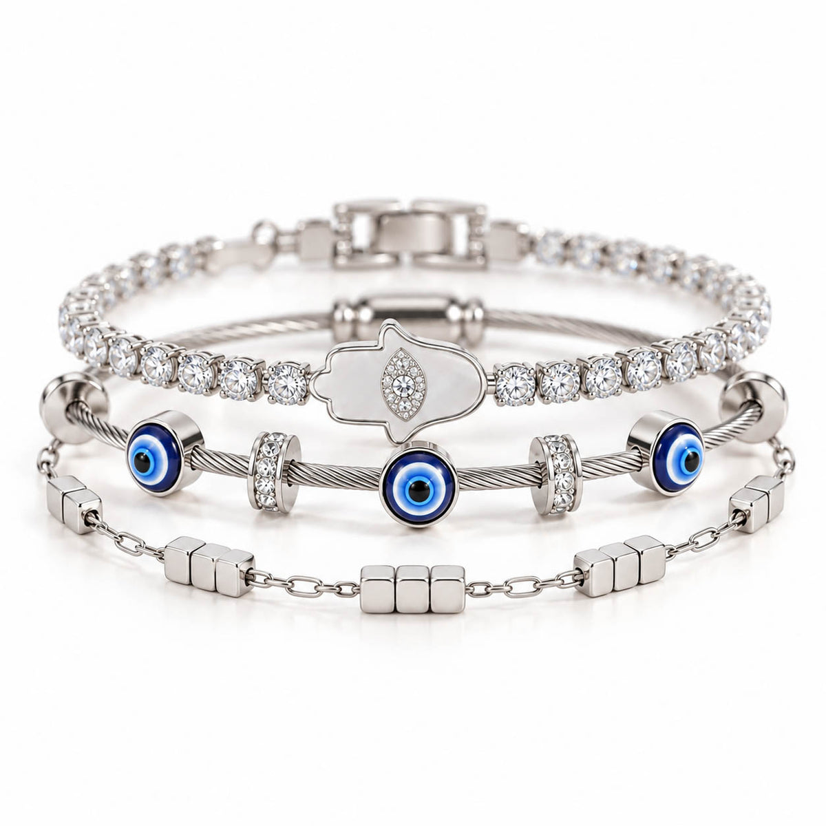 A product photo of a stacked set of silver-tone bracelets featuring a crystal tennis chain with a mother-of-pearl Hamsa hand pendant, a twisted cable wire band with blue evil eye beads, and a link chain with small cube charms.
