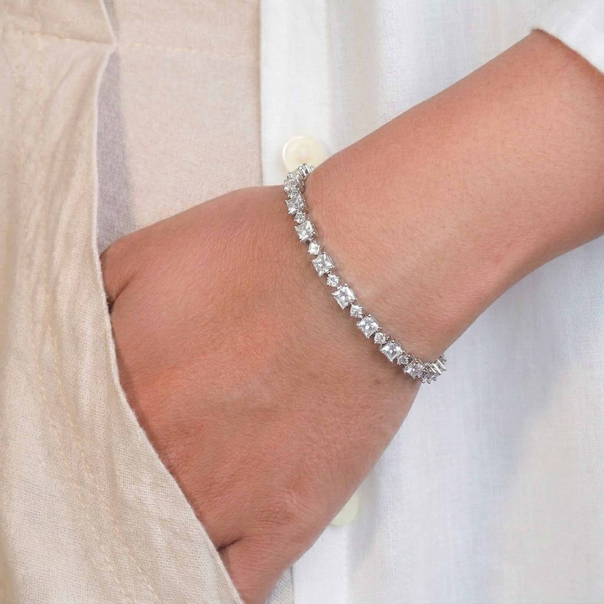 Wrist-worn silver tennis bracelet featuring round-cut cubic zirconia stones in a classic linked design.