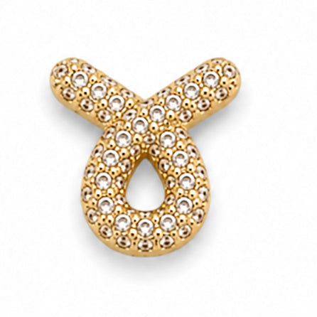 Gold-tone Taurus zodiac charm featuring the distinctive bull-horn symbol with a rounded looped design. The charm is intricately covered with numerous small white rhinestones, creating a sparkling textured surface. It has polished gold-tone edges, raised detailing, and a sleek dimensional finish, isolated against a clean white background.

