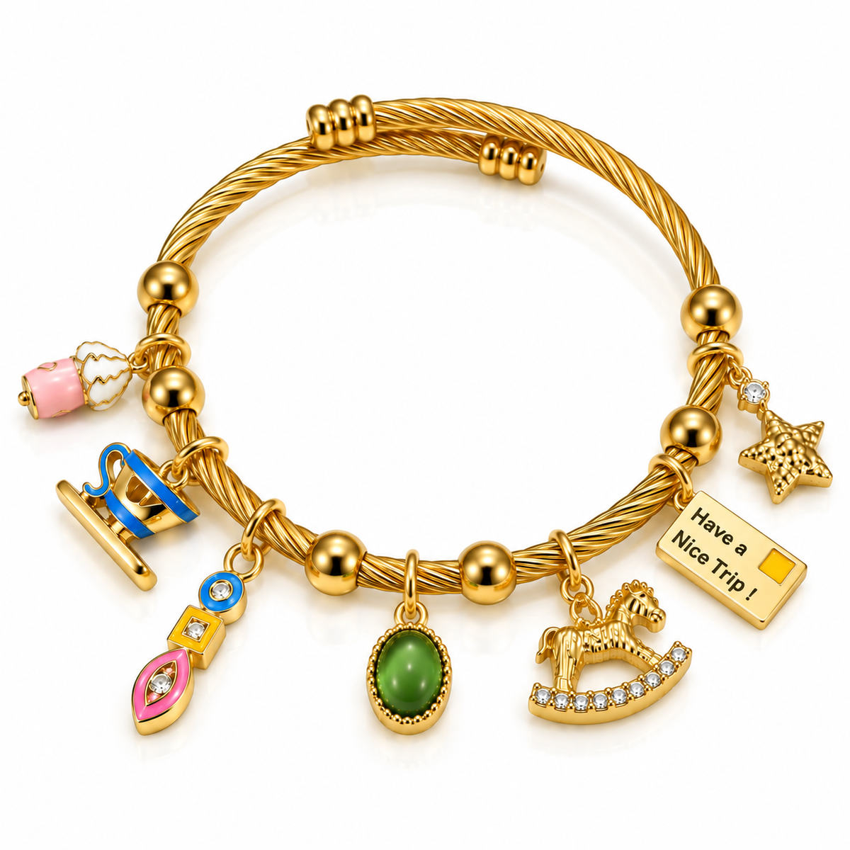 Gold-toned twisted wire charm bracelet featuring a pink perfume bottle, blue suitcase, colorful geometric charm, green gemstone, rocking horse, star, and “Have a Nice Trip!” travel tag on a white background.
