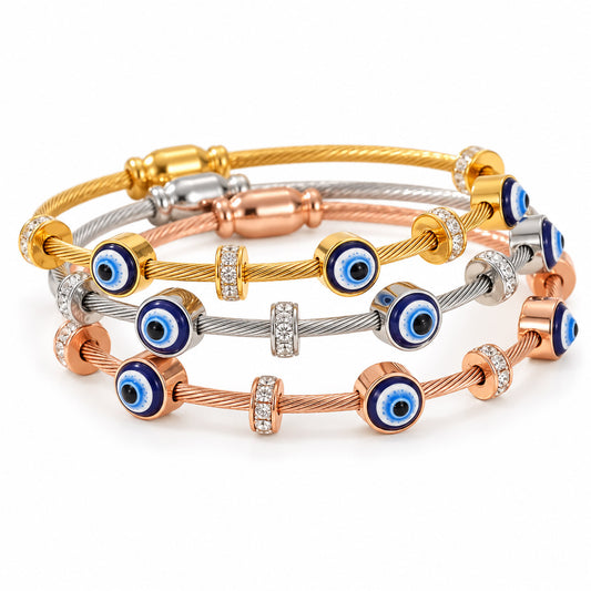 A product photo of a stacked set of tri-color twisted cable wire bracelets featuring yellow gold, silver, and rose gold finishes, adorned with alternating blue-and-white enamel evil eye charms and rhinestone spacers.